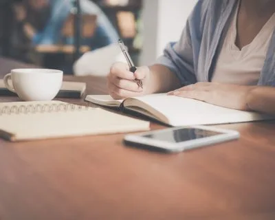 Person writing a will in a notebook with a smartphone and coffee on the desk