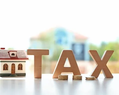 Word TAX, house model and coins on table against blurred background