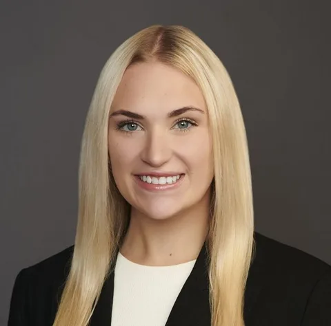Elise Wente smiling, wearing a black blazer and white top, with long blonde hair against a gray background.