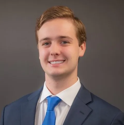 Grant Barlow in a blue suit and tie, smiling against a plain gray background.