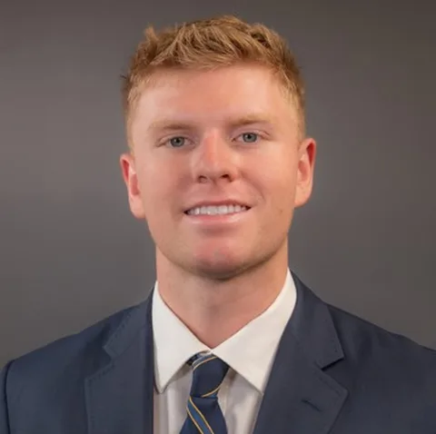 Tye Wydner in a suit with a white shirt and blue striped tie, smiling against a plain background.