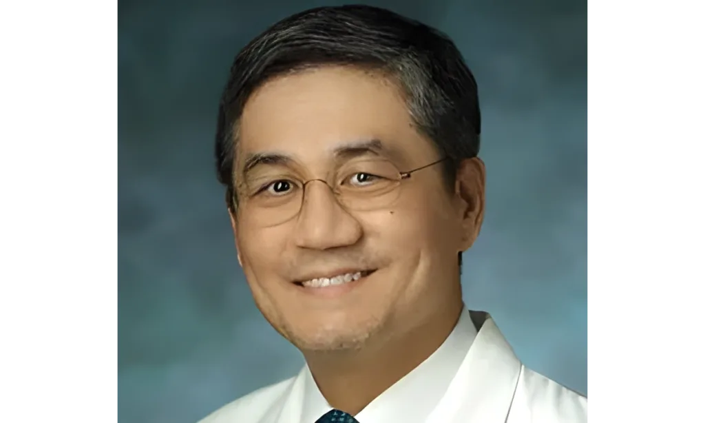 Smiling man in glasses and a white coat against a blue background.