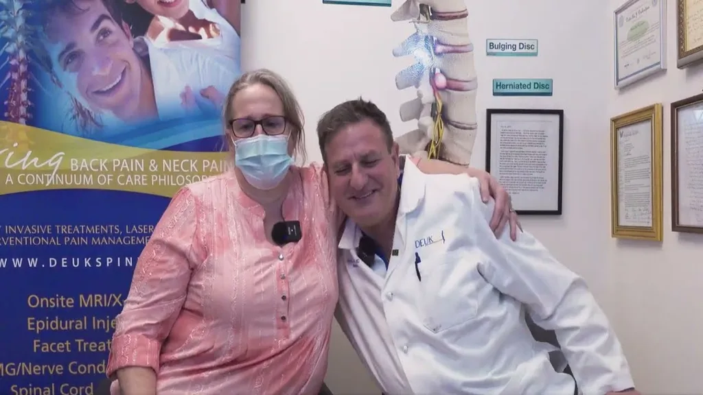 A masked woman and a man in a lab coat smiling and posing together in a medical office.