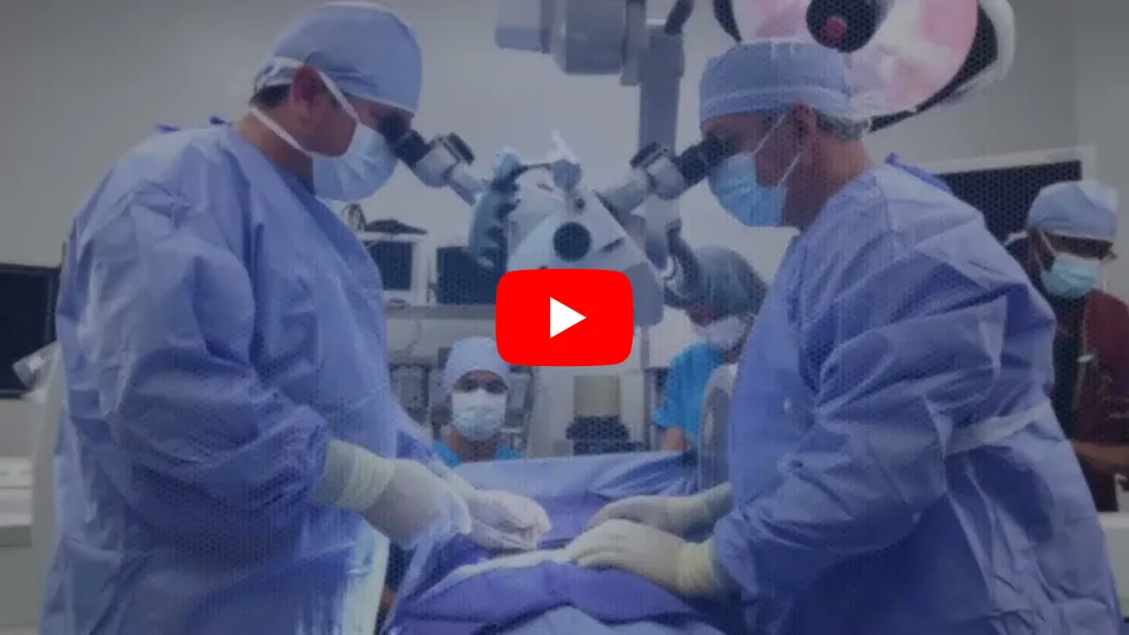 Surgeons in blue gowns and masks perform surgery under a microscope in an operating room.