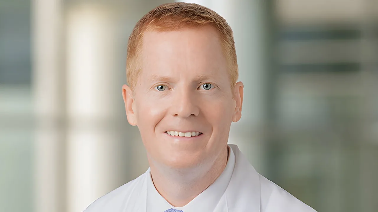 Smiling person in a white coat against a blurred background.