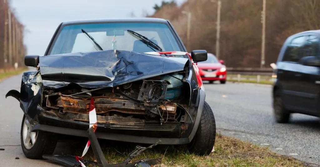 Severely damaged vehicle with a crushed front end parked on the roadside after a major accident, awaiting emergency roadside assistance or towing services