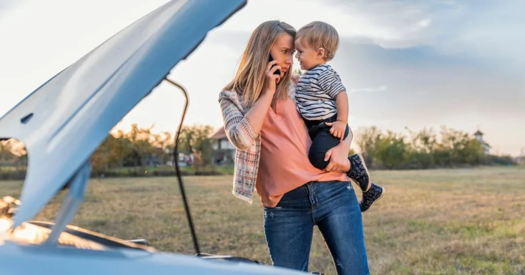 Holiday Road Trip Rescue: Your Emergency Guide for Maryland and Virginia Travel 3 A woman holding a young child while making a phone call next to her broken-down car with the hood open, seeking roadside assistance.