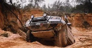 Off-road SUV stuck at an angle on rugged, muddy terrain in a canyon-like area, showing the need for off-road recovery assistance.