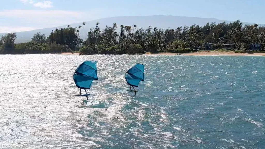 462 Laulea Place, The Ultimate Home Base for Water People 3 two people wing foiling off the coast of Spreckelsville on Maui's North Shore. Haleakala volcano can be seen in the distance behind the palm tree lined beach.