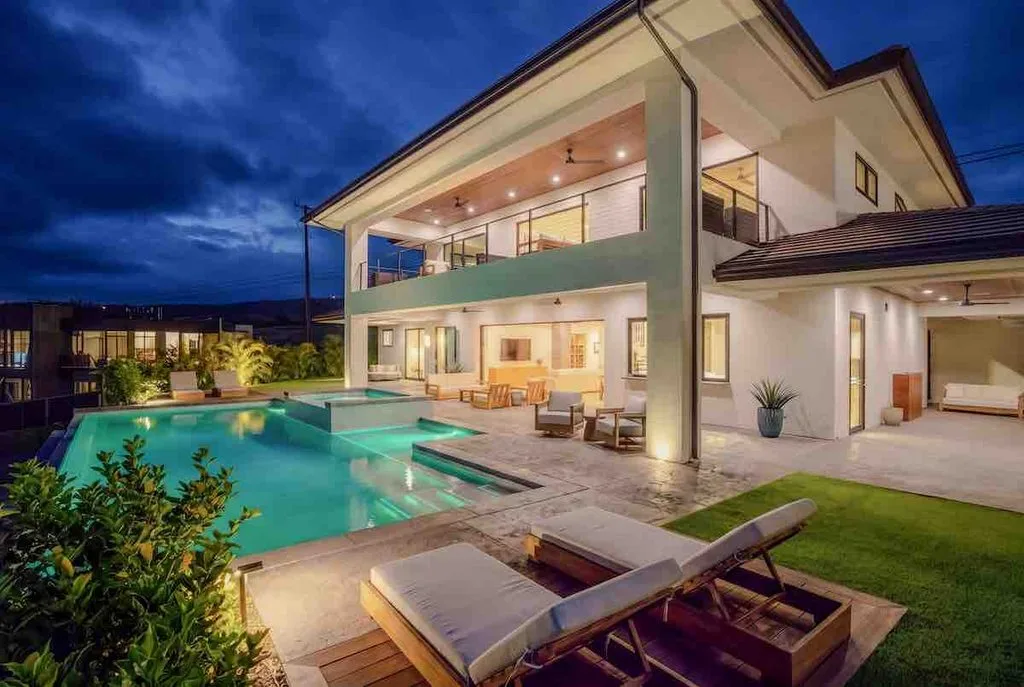 Evening and 22 Halapa Place in Wailea Ridge. The two story luxuty home and its pool area are fully illuminated. A couple of pool side lounge chairs are in the foreground. 