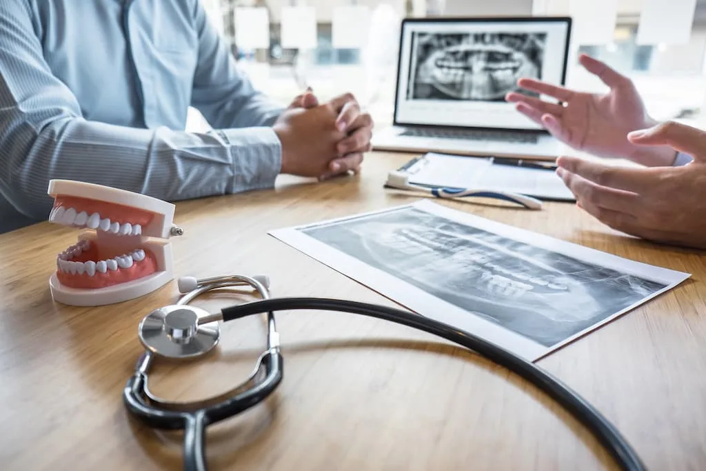 5 tooth replacement options: cost, comfort & longevity guide 6 two people discussing dental x-rays with a model jaw and stethoscope on the table.
