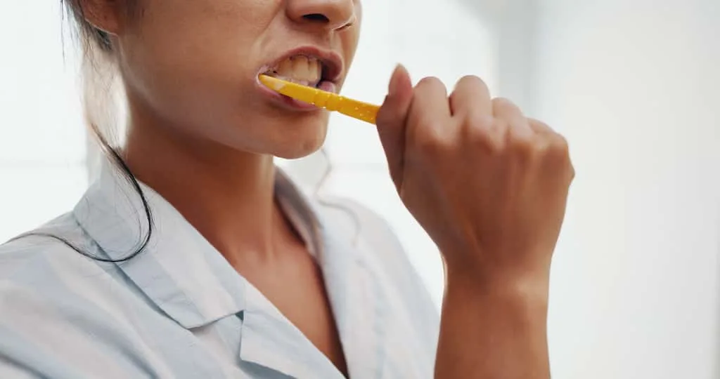 gum recession signs: recognizing the early warnings your mouth is sending 3 person brushing their teeth with a yellow toothbrush.