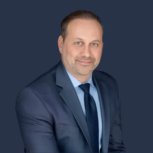 Man in a blue suit and tie against a dark background.