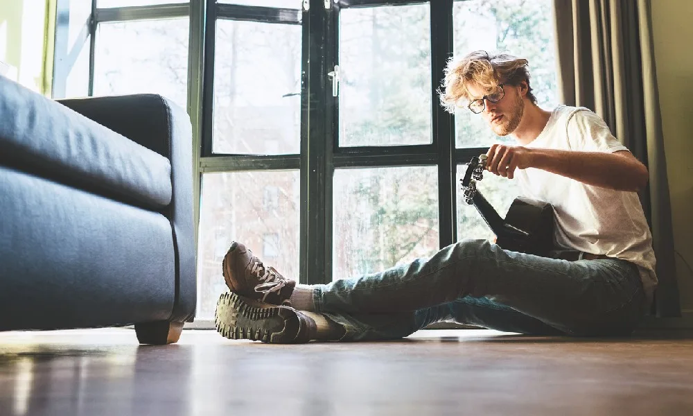 A musician sits on the floor and shows how to tune a guitar.