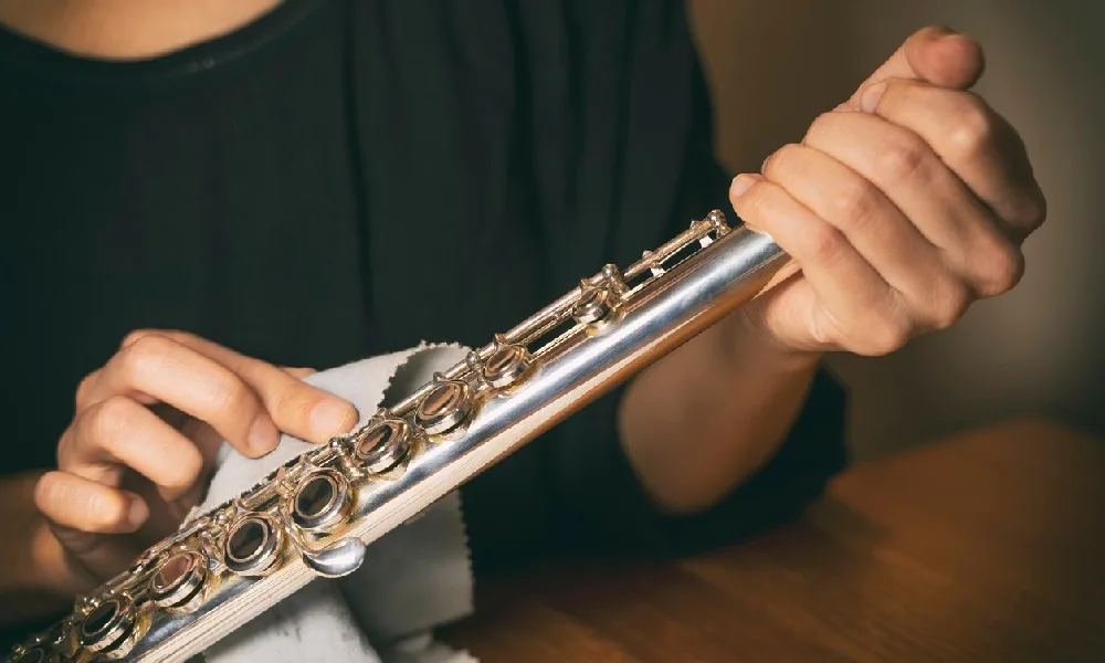 A flute player cleans an instrument with a polishing cloth.