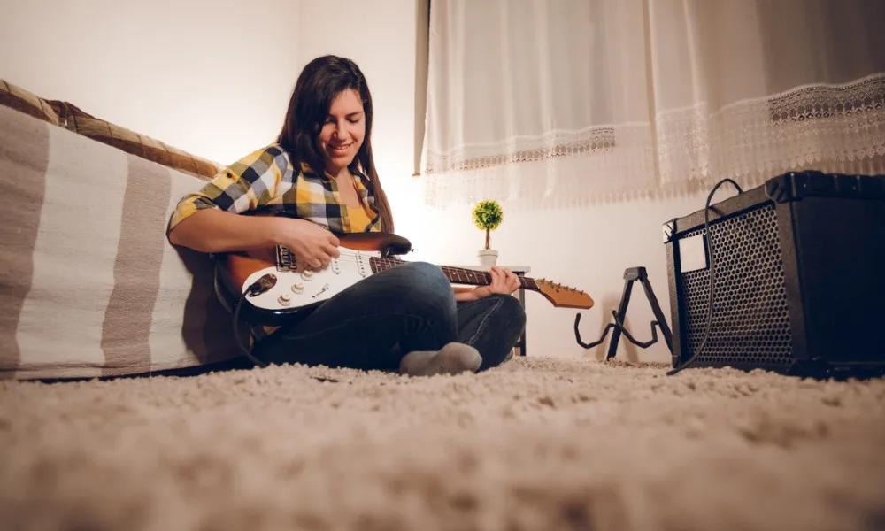 A female guitarist plays a guitar plugged into a combo guitar amp.