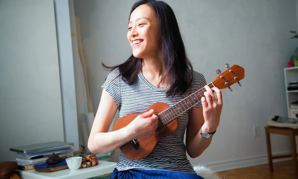 How to Tune a Ukulele 23 A young woman smiles while she plays her ukulele.