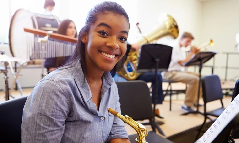 Girl smiling while holding a saxophone during her woodwinds lessons