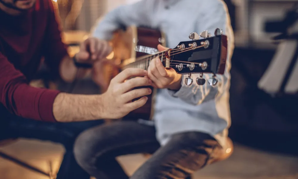 Man teaching a young boy to play a Yamaha acoustic guitar.