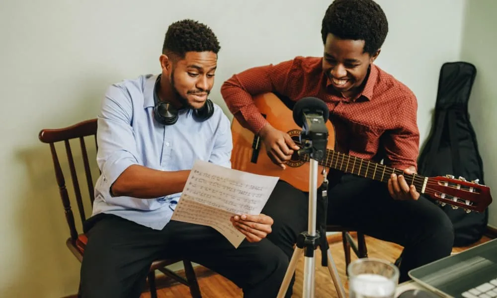 A multiple-instrument player teaching a student to play guitar in a music studio.