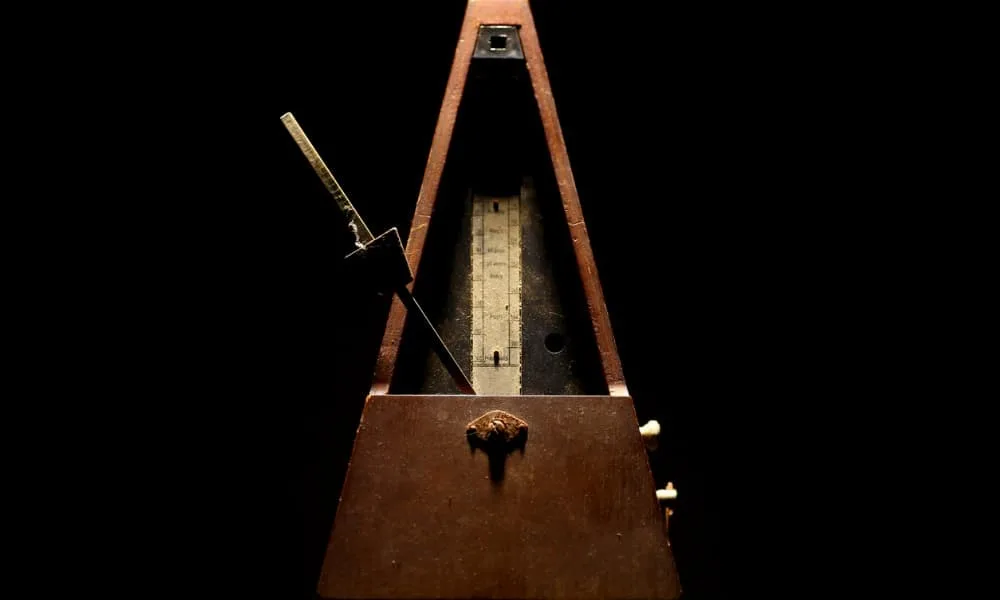 Feed Your Rhythmic Intelligence and Improve Your Sense of Rhythm 10 A wooden metronome used to improve rhythm sits on a black background.