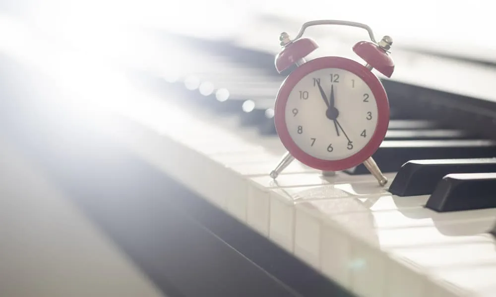 How Long Are Piano Lessons? Determining the Length, Frequency, and Duration 1 A old-fashioned red alarm clock sitting on piano keys, prompting the question, “How long are piano lessons?”