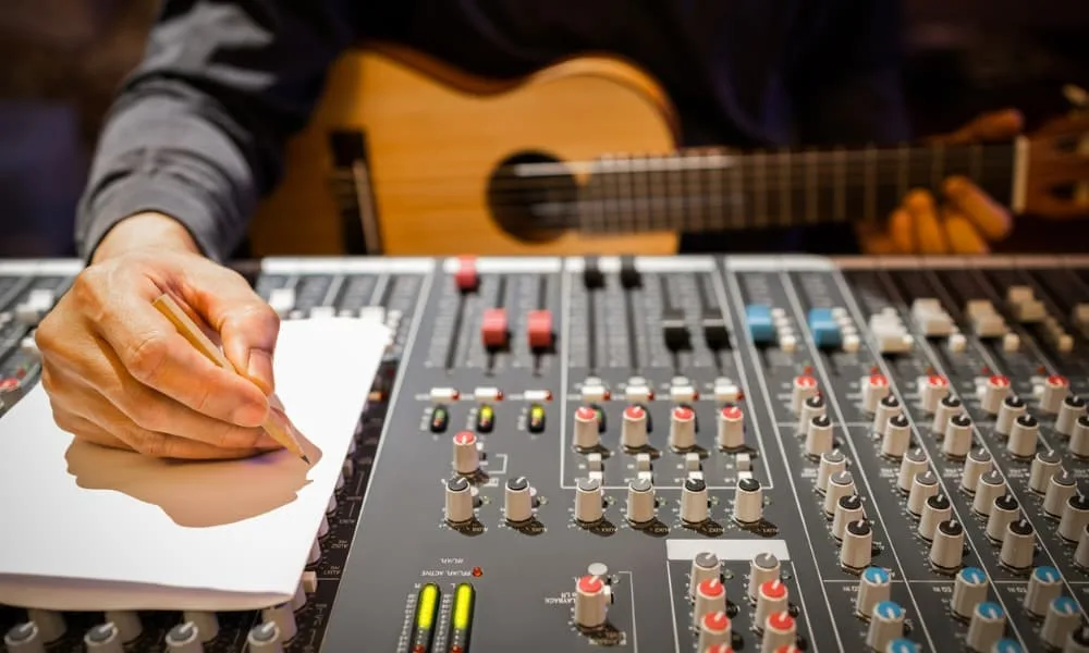 The Secret to Writing Amazing Musical Bridges 8 Male composer hands writing a bridge of a song on white paper in a recording studio.