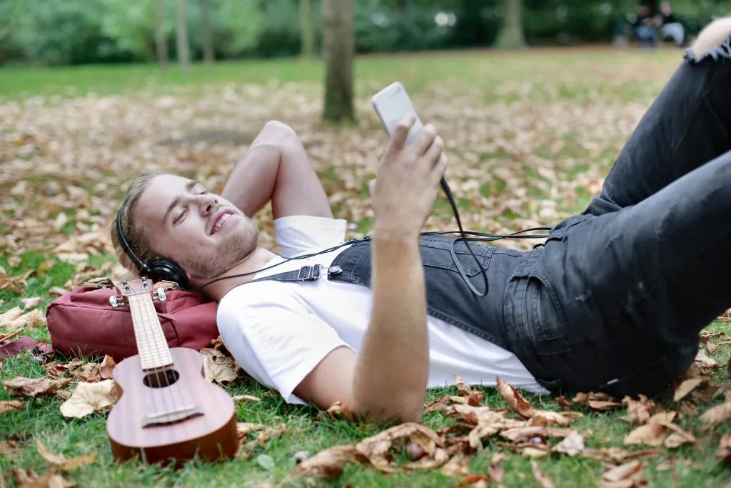 9 Ways to Tap into the Power of Relaxing Music to Reduce Stress 13 man listening to relaxing music while lying down in a park