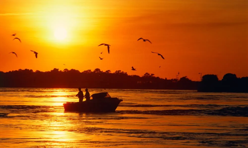 two people fishing at sunset from a boat