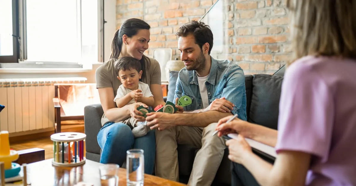 Smiling parents with their young child engaging with a counselor during a supportive couples counseling session for parents.